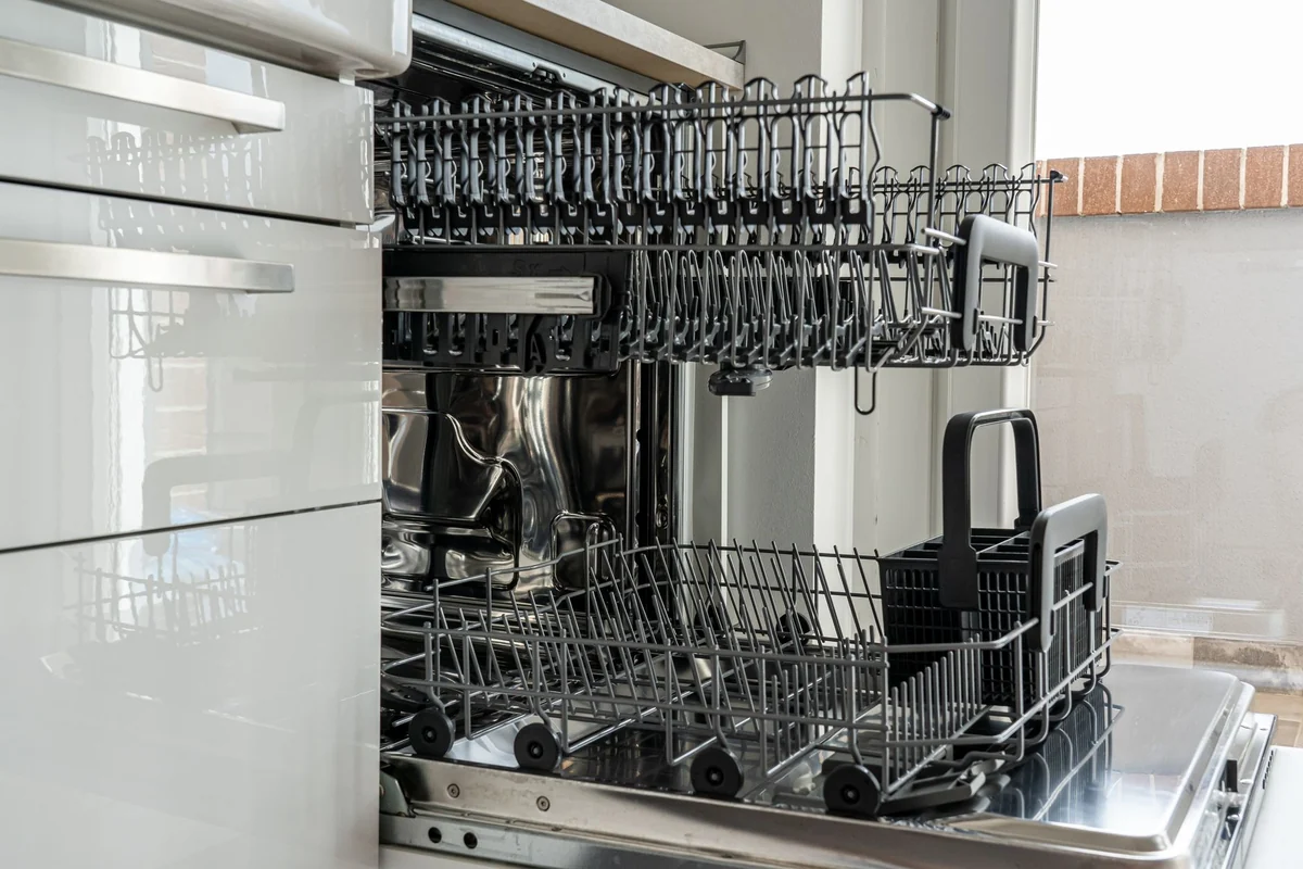 Lave-vaisselle encastrable ouvert et vide dans une cuisine claire, paniers en place