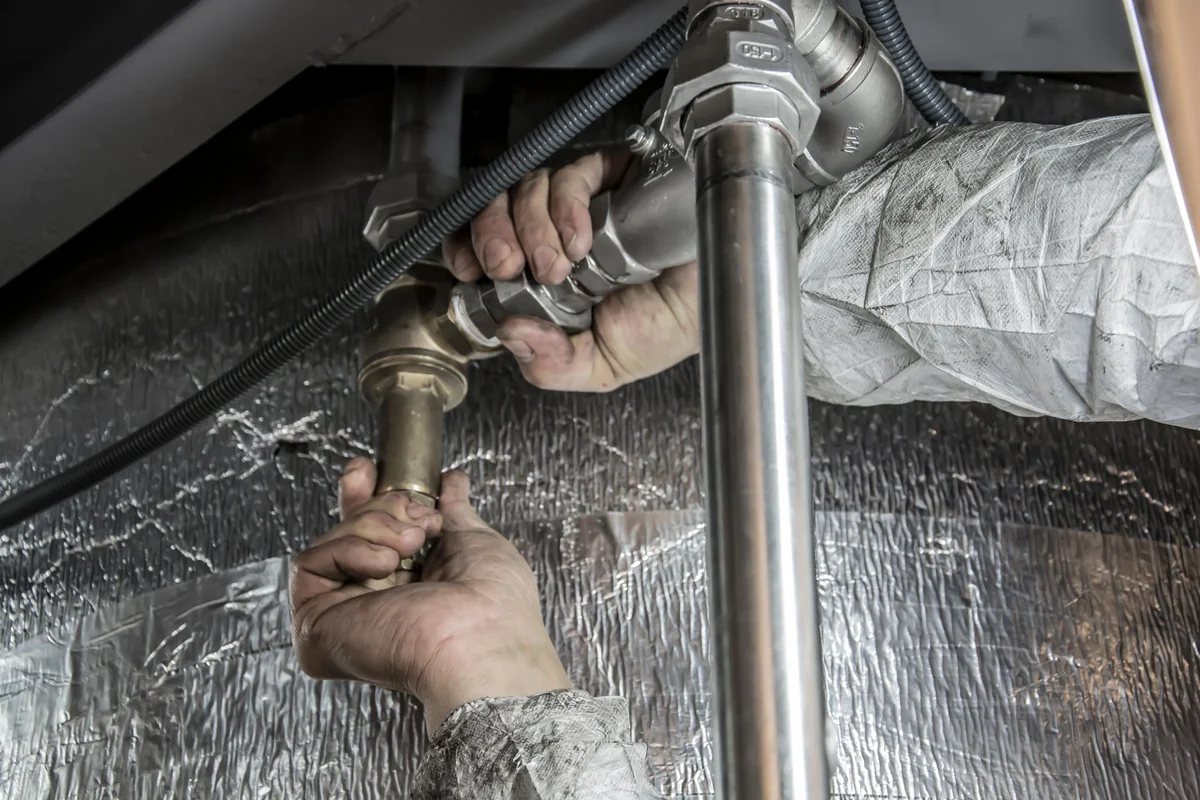 Mains serrant un raccord de canalisation sous un évier, démontage du siphon